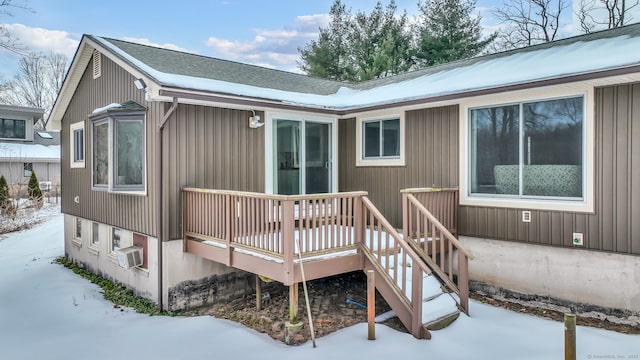 snow covered house with a wooden deck, cooling unit, and roof with shingles