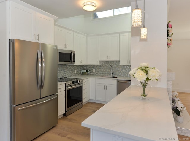 kitchen with hanging light fixtures, decorative backsplash, appliances with stainless steel finishes, white cabinets, and a sink