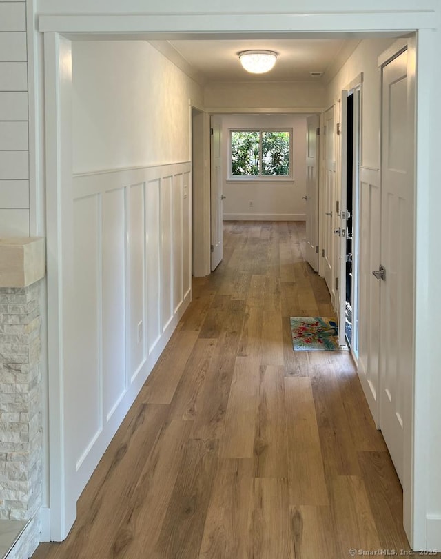 hallway with crown molding, a wainscoted wall, a decorative wall, and light wood-style flooring