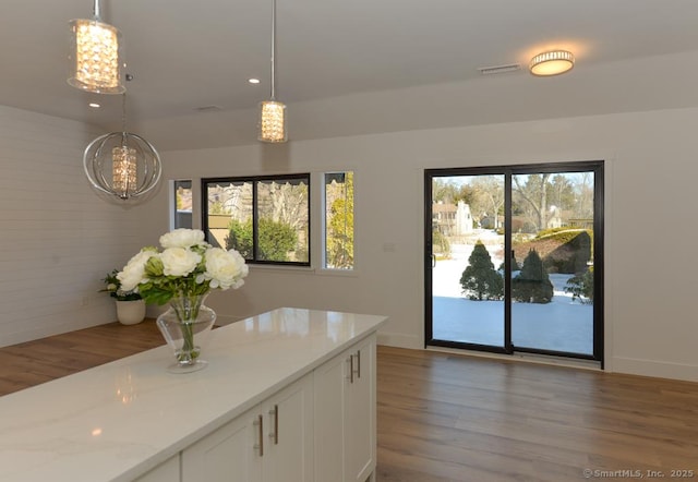 kitchen featuring wood finished floors, white cabinets, decorative light fixtures, and light stone countertops