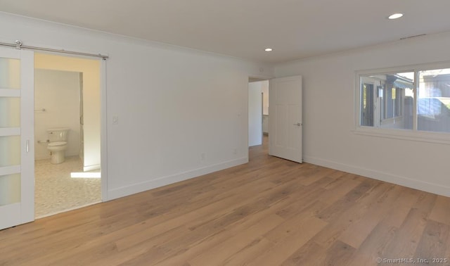 unfurnished room with light wood finished floors, a barn door, baseboards, and recessed lighting