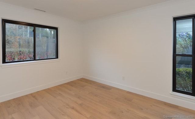 empty room featuring light wood-style floors, visible vents, ornamental molding, and baseboards