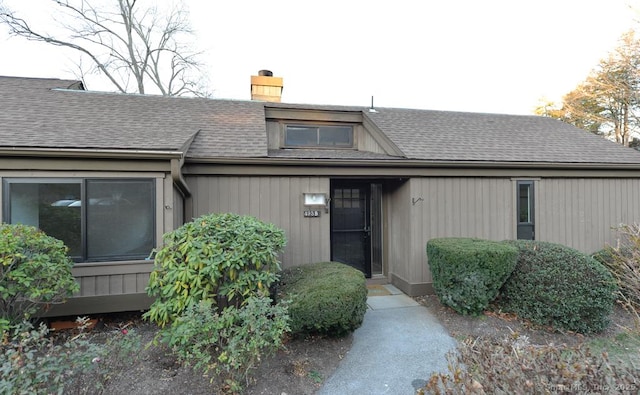 view of exterior entry featuring a chimney and roof with shingles
