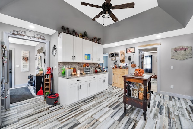 kitchen featuring light stone counters, backsplash, white cabinetry, and baseboards