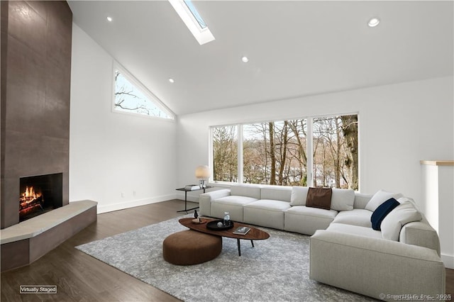 living area with dark wood-style floors, a skylight, a fireplace, recessed lighting, and high vaulted ceiling