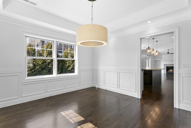 unfurnished dining area featuring a warm lit fireplace, a decorative wall, dark wood finished floors, wainscoting, and ornamental molding