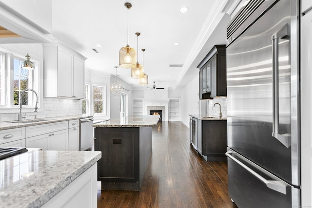 kitchen featuring appliances with stainless steel finishes, a sink, ornamental molding, a warm lit fireplace, and decorative backsplash