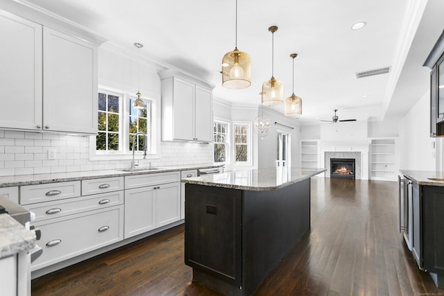 kitchen featuring a sink, ceiling fan, open floor plan, a kitchen island, and a glass covered fireplace