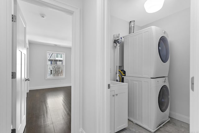 washroom with stacked washing machine and dryer, baseboards, and wood finished floors