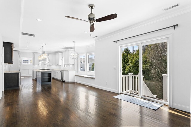 unfurnished living room with a ceiling fan, a chandelier, a sink, dark wood-style floors, and crown molding