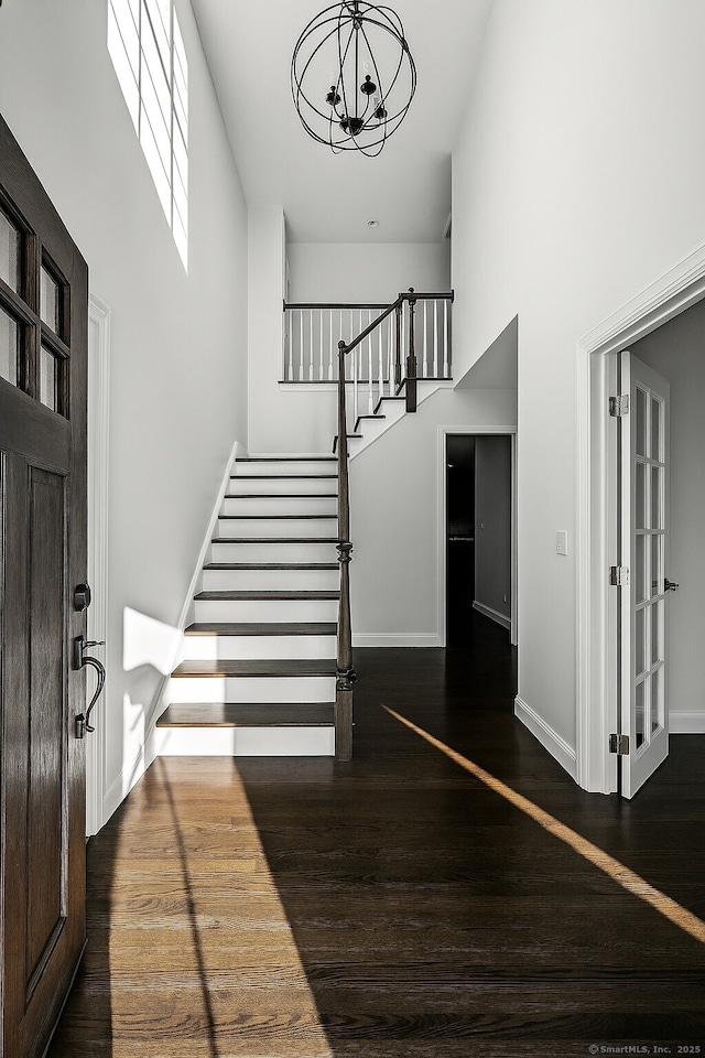 entryway with stairway, wood finished floors, baseboards, a chandelier, and a high ceiling