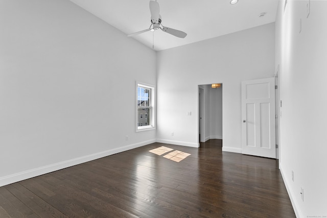 empty room featuring a ceiling fan, a towering ceiling, baseboards, and dark wood finished floors