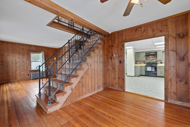 stairway with baseboards, a ceiling fan, hardwood / wood-style flooring, radiator heating unit, and wood walls