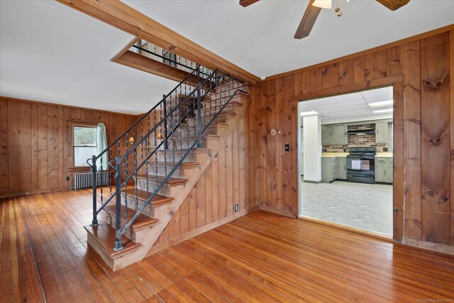 stairs featuring baseboards, ceiling fan, wooden walls, wood-type flooring, and radiator heating unit