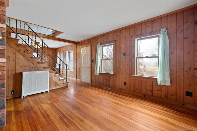 foyer entrance with wooden walls, visible vents, stairway, radiator, and hardwood / wood-style floors