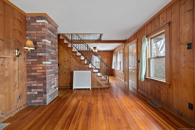 entrance foyer featuring wooden walls, visible vents, radiator heating unit, hardwood / wood-style floors, and stairs