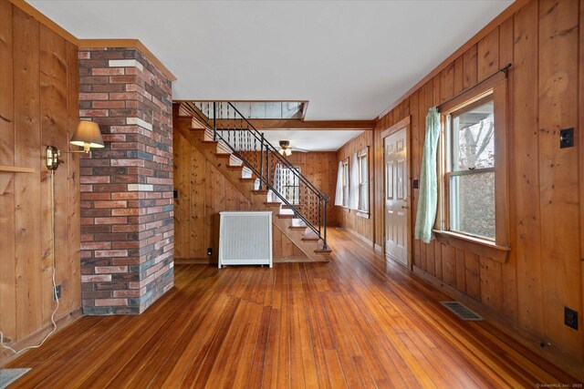 entrance foyer featuring radiator heating unit, visible vents, stairway, wooden walls, and hardwood / wood-style flooring
