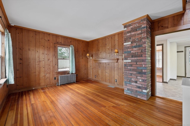 spare room featuring baseboards, wood walls, hardwood / wood-style floors, and radiator heating unit