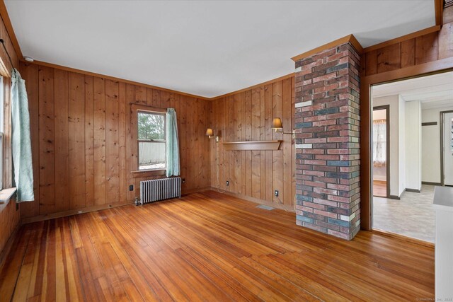 unfurnished living room featuring wooden walls, wood-type flooring, radiator heating unit, and baseboards
