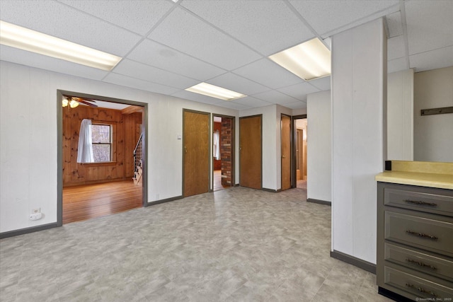 unfurnished room with a paneled ceiling, wood walls, baseboards, and light floors