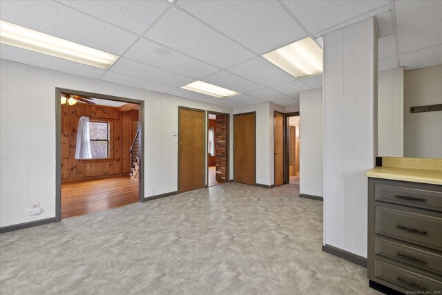 interior space with wood walls, a paneled ceiling, baseboards, and light floors