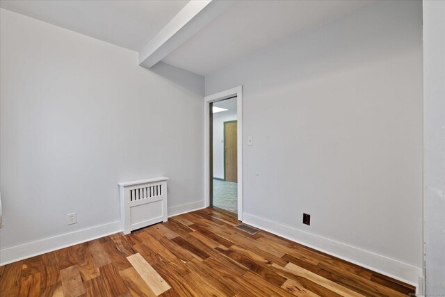 empty room with baseboards, beamed ceiling, and wood finished floors