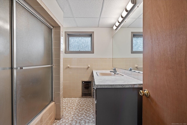 full bathroom featuring a healthy amount of sunlight, a paneled ceiling, tile walls, and vanity