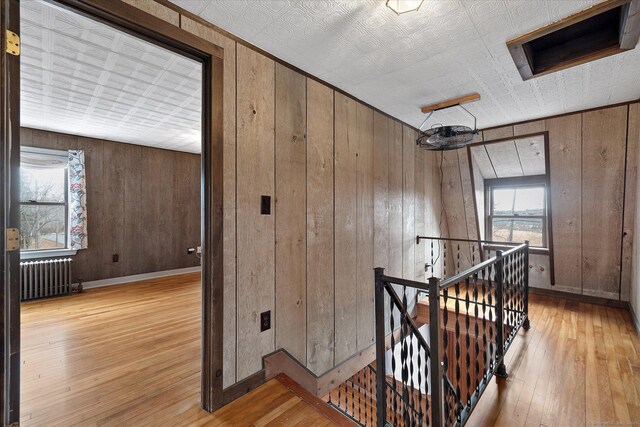 hall with wood walls, an upstairs landing, hardwood / wood-style floors, and radiator
