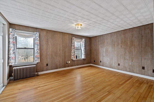 empty room featuring wood walls, baseboards, radiator, and wood finished floors