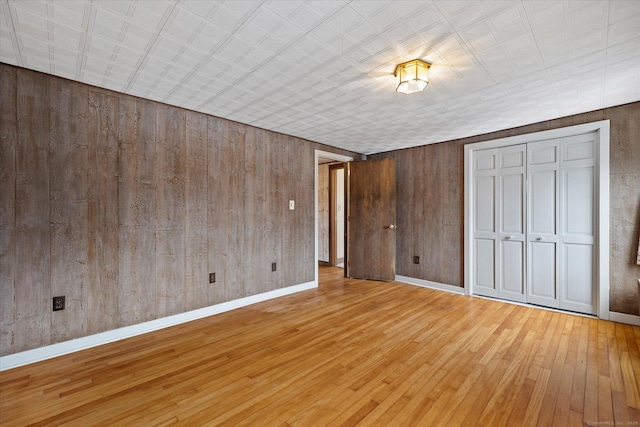 unfurnished bedroom with hardwood / wood-style floors, wood walls, a closet, and baseboards