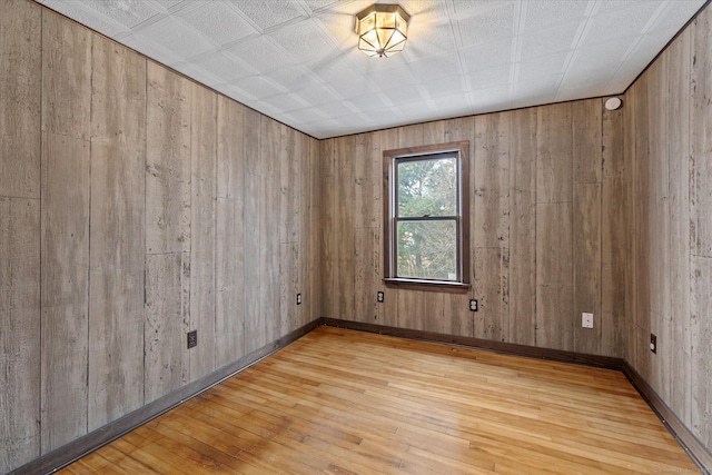 spare room with wood-type flooring, wooden walls, and baseboards