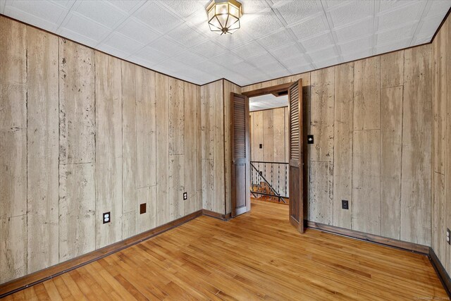 unfurnished room featuring wood walls, wood-type flooring, and baseboards