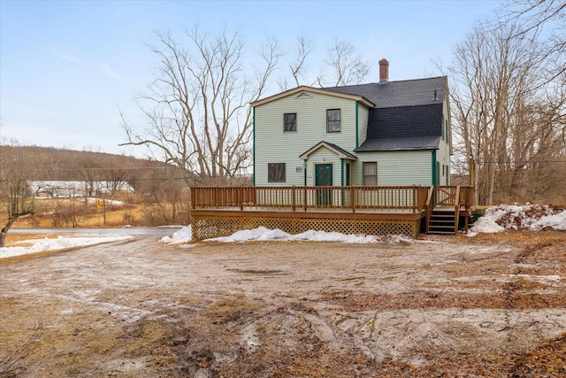 snow covered rear of property with a chimney, roof with shingles, and a deck