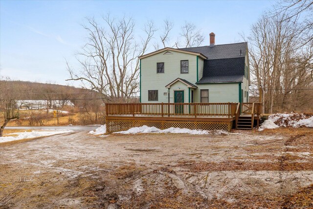 snow covered rear of property with a wooden deck, a chimney, and a shingled roof