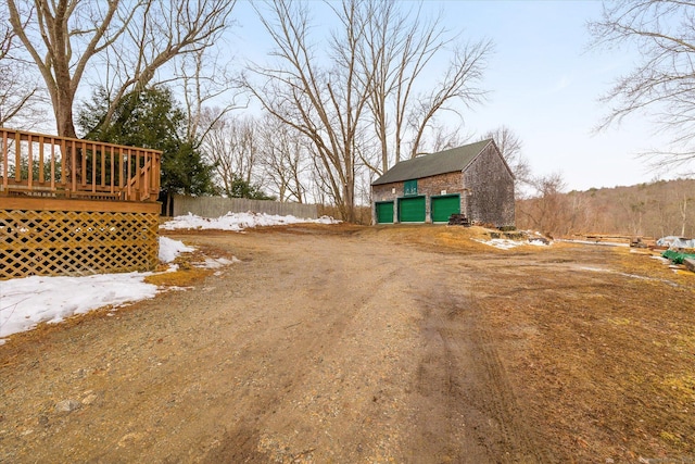 view of yard with a garage, dirt driveway, an outbuilding, and a wooden deck