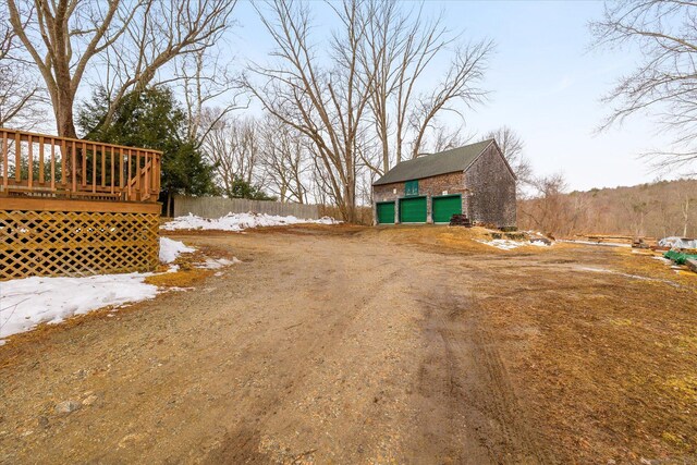 view of yard featuring an outbuilding, a garage, a wooden deck, and dirt driveway