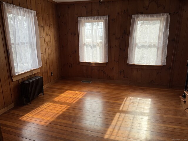 unfurnished room featuring radiator, visible vents, hardwood / wood-style floors, wooden walls, and baseboards