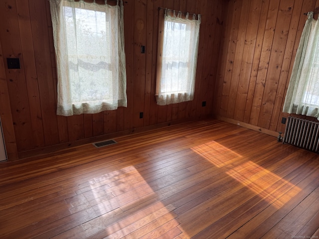 empty room featuring wood walls, visible vents, baseboards, radiator, and hardwood / wood-style floors