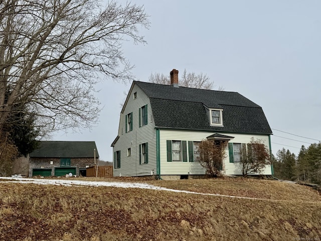 colonial inspired home with roof with shingles, a chimney, and a gambrel roof