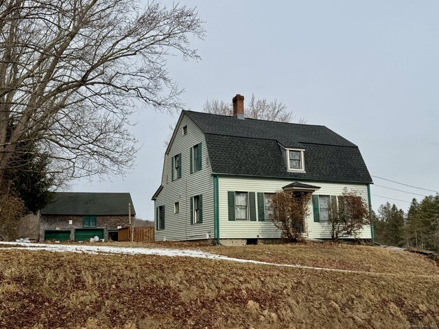 colonial inspired home featuring roof with shingles, a gambrel roof, and a chimney