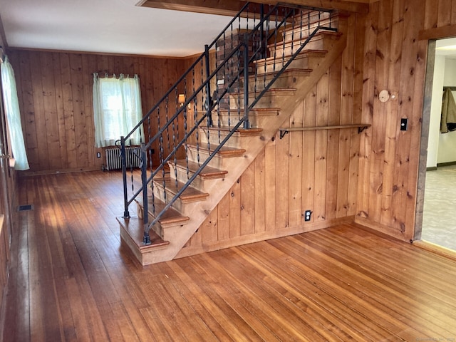 stairway featuring wood-type flooring, baseboards, wood walls, and radiator heating unit