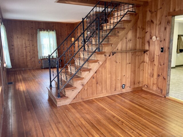 stairs featuring wood-type flooring, baseboards, radiator, and wood walls