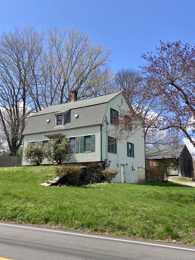 colonial inspired home featuring a gambrel roof, a shingled roof, a front lawn, and a chimney
