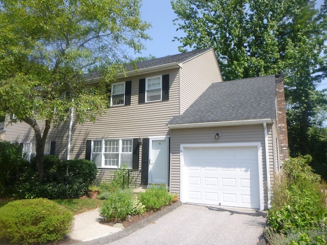 colonial house with a garage, a shingled roof, and aphalt driveway