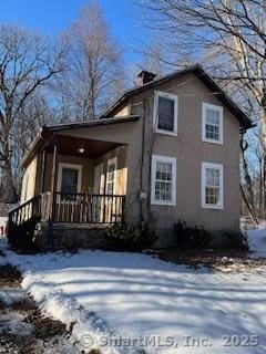 view of front facade featuring covered porch, a chimney, and stucco siding