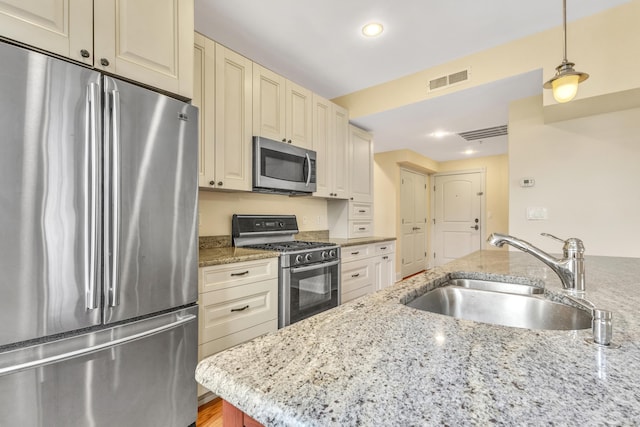 kitchen with a sink, visible vents, appliances with stainless steel finishes, cream cabinetry, and pendant lighting