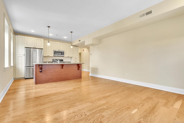 kitchen featuring stainless steel appliances, light wood finished floors, a kitchen bar, and visible vents