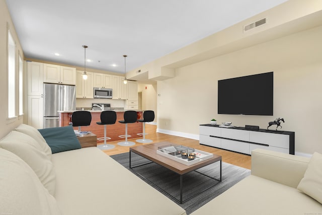 living area with light wood-style flooring, visible vents, baseboards, and recessed lighting