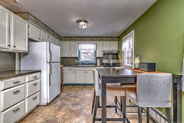 kitchen featuring dark countertops, freestanding refrigerator, stainless steel electric stove, white cabinetry, and a sink