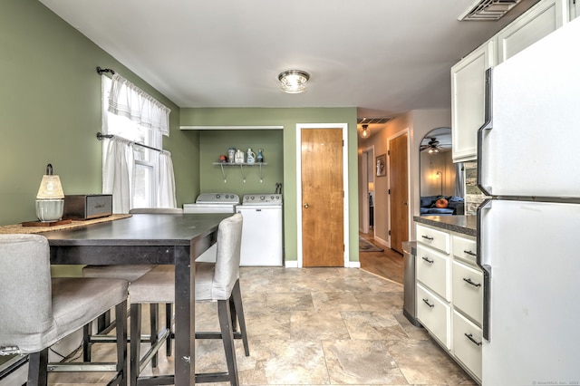 kitchen with dark countertops, visible vents, freestanding refrigerator, white cabinetry, and washer and dryer